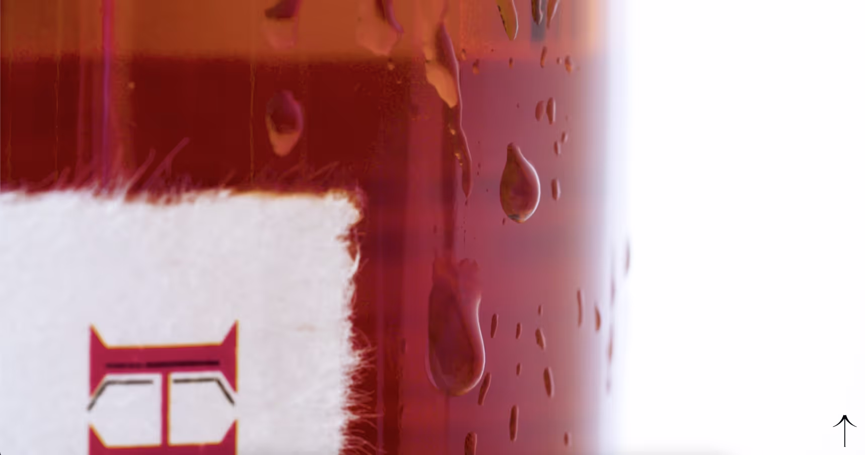 A frame from Hayashi Whisky video reel displayed on the home page of the website. Extreme close-up detail of Hayashi whisky branding showing part of a red lettermark against white, with condensation or water droplets on glass surface.